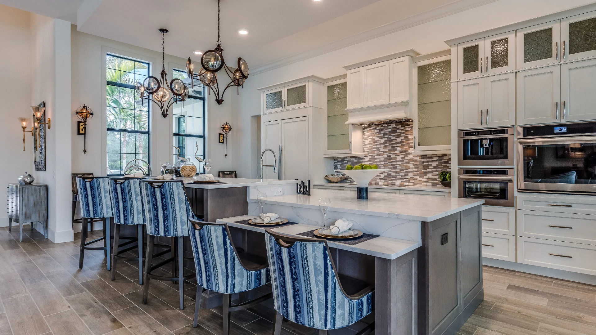 This image is showing a modern luxury kitchen with custom white cabinetry, marble countertops, and a stylish island seating area.